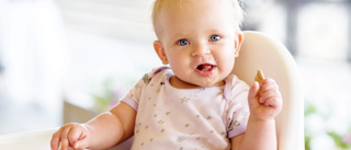 Baby i en høj stol der spiser selv