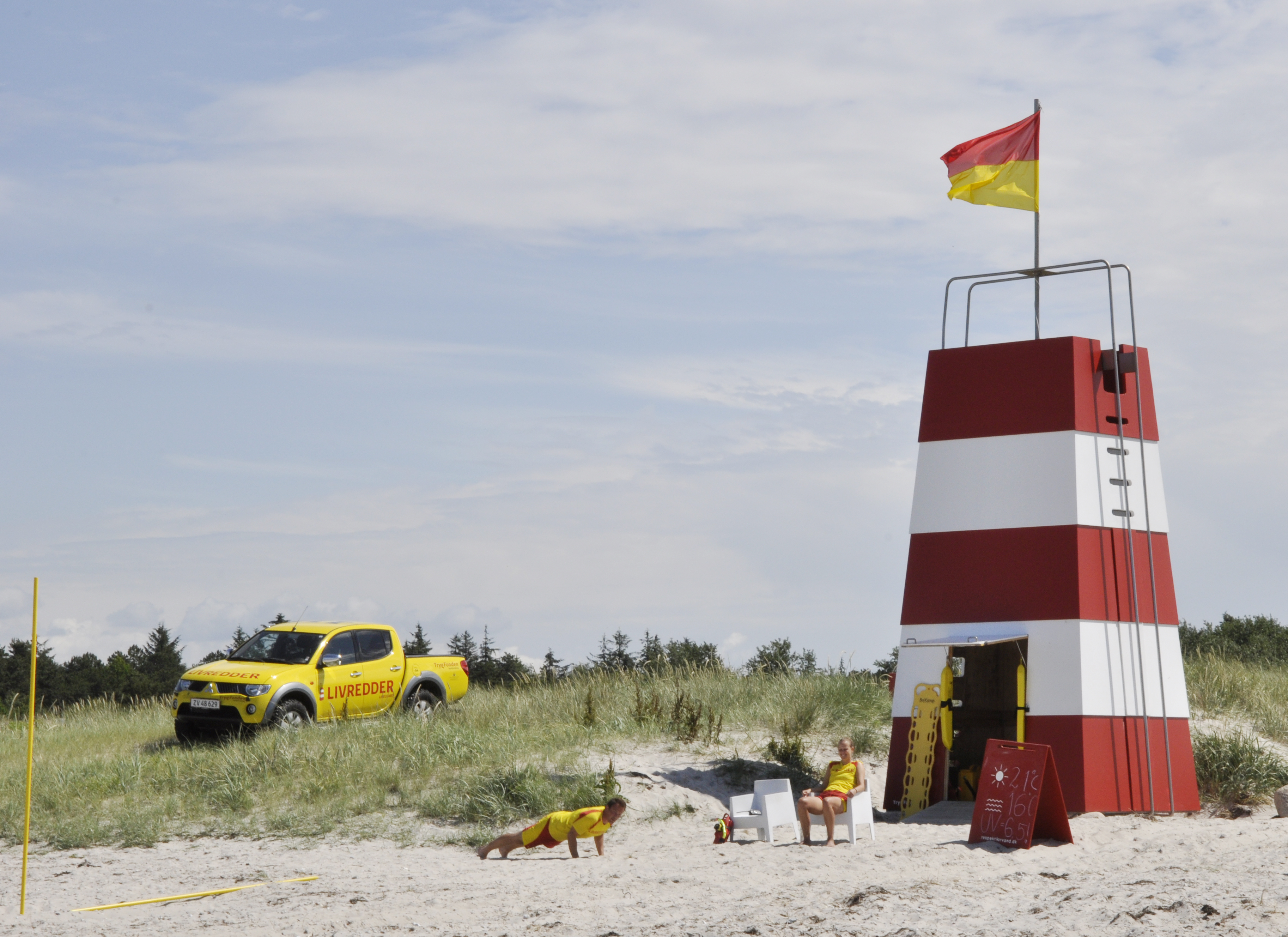 Stranden med rødt/hvidt livreddertårn med gul pickup i baggrunden
